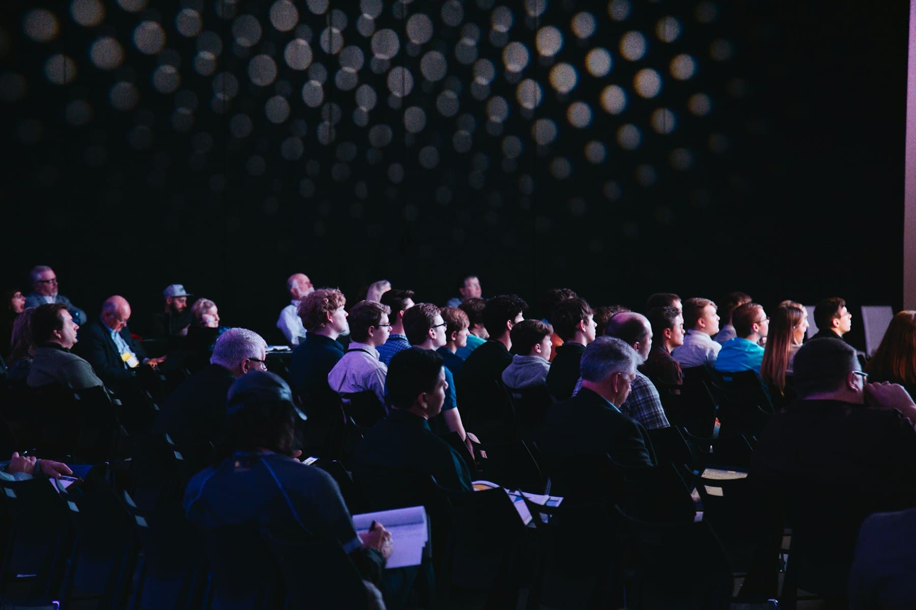 A darkened conference audience lit by the stage